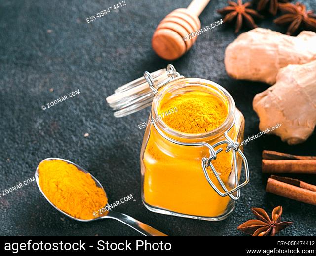 Dried turmeric powder in glass jar and spoon on black cement background.Ingredients for golden milk, turmeric latte, detox drink