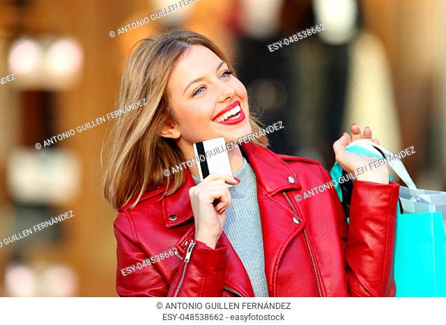 Portrait of a fashion shopper thinking and looking at side holding a credit card with a store in the background