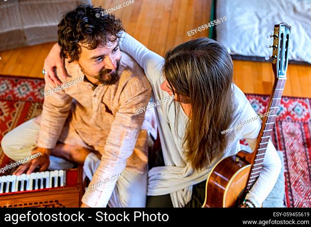 Young shamanic man and woman holding classical guitar and playing harmonium for silent meditation and prayer while looking at each other with love