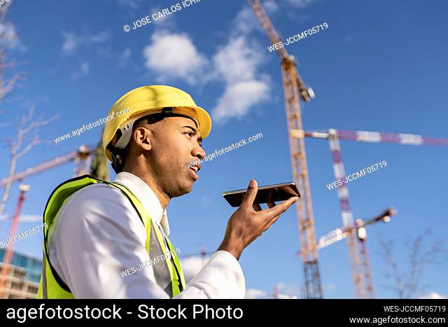 Engineer talking on smart phone through speaker at construction site on sunny day