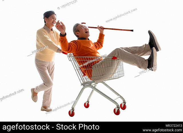 A happy old man pushes his wife sat in the shopping cart