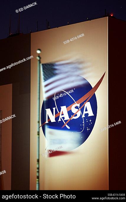 American flag and flag of Space Shuttle Endeavour in foreground with large NASA insignia on the side of the Vehicle Assembly Building (VAB) at NASA Kennedy...