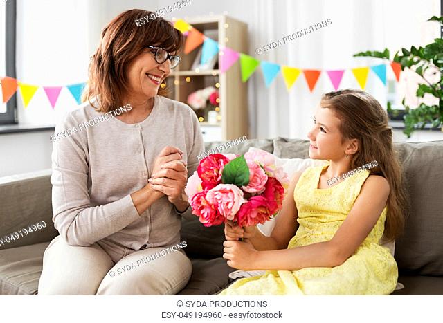 granddaughter giving grandmother flowers at home
