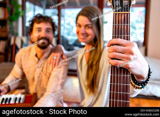 Shamanic man and woman holding classical guitar with nylon strings and man playing harmonium for sacred and kirtan music looking at camera