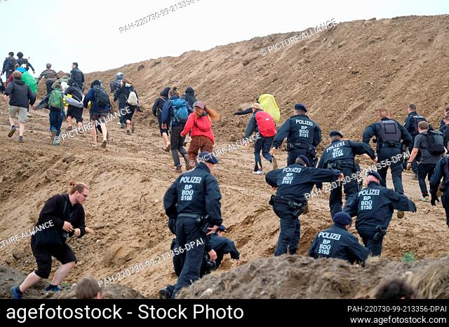 30 July 2022, Saxony, Schkeuditz: Climate activists and police officers walk up the hill of a construction site of the logistics company DHL at Leipzig-Halle...