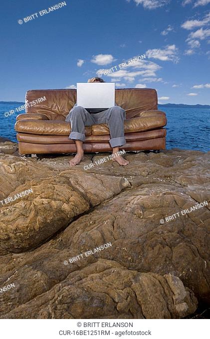 man on couch at beach with laptop