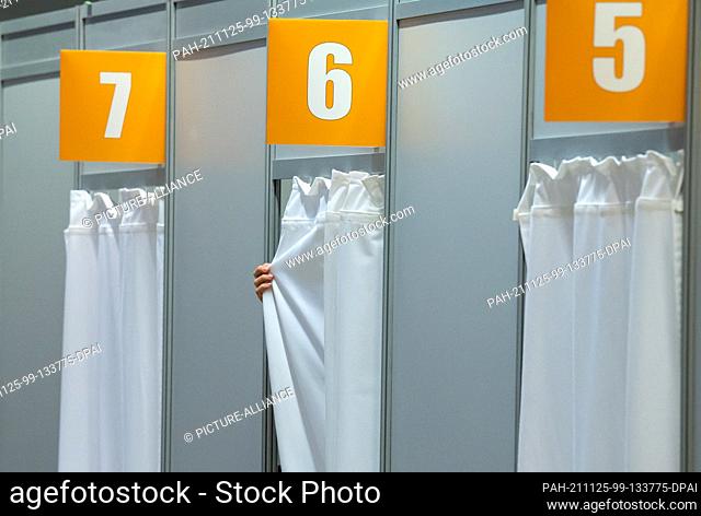 24 November 2021, Berlin: A helper pulls the curtain of a vaccination booth at the Corona Vaccination Center Berlin-Tegel