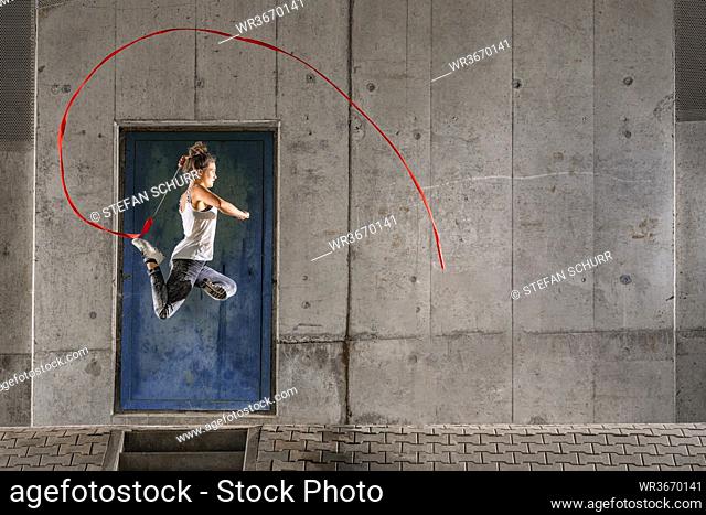 Woman holding ribbon practicing rhythmic gymnastics against wall under bridge