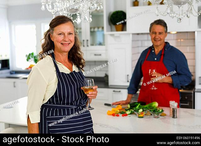 Portrait of happy senior caucasian couple in kitchen cooking together, drinking wine