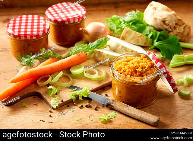 Glass jars filled with fresh vegetable conservation placed on wooden table with carrots and celery in light kitchen during cooking process