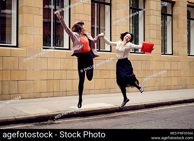 Cheerful businesswoman jumping with colleague on street