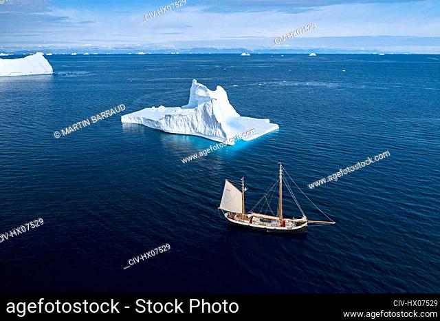 Ship sailing past iceberg on sunny blue Atlantic Ocean Greenland
