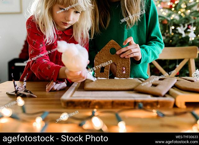 Sisters decorating gingerbread house at home