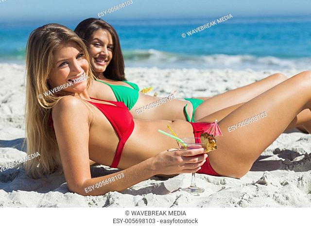 Cheerful tanned blonde and brunette taking sun drinking cocktails