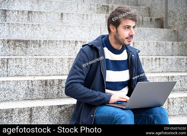 Handsome hipster modern businessman, using laptop in the city, with positive expression