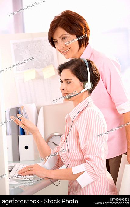 Customer care operator working at desk with supervisor, smiling