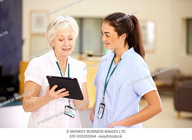 Female Consultant In Meeting With Nurse Using Digital Tablet