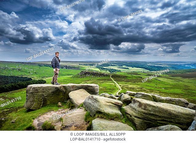 A rambler on Higger Tor in the Derbyshire Peak District with Carl Wark in the middle distance
