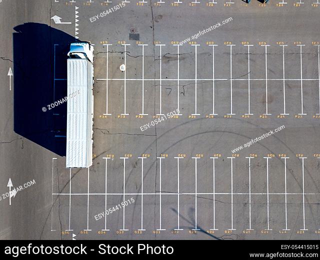 Aerial view from a flying drones of parking lot, marking parking spaces with a long truck and long shadows from it on a summer day. Top view