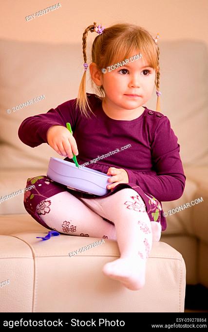 Little girl in purples dress, playing with plastic toy dishes, sitting on couch at home