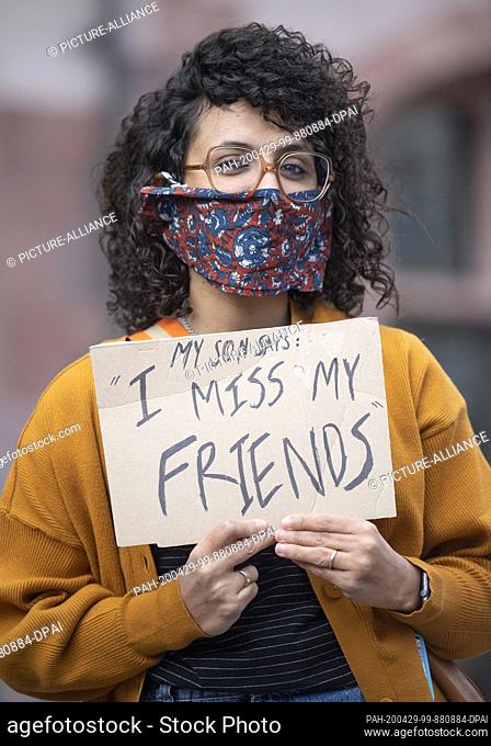 29 April 2020, Hessen, Frankfurt/Main: A young woman who has her nose and mouth covered shows a poster with the inscription ""My son says: I miss my friends""...