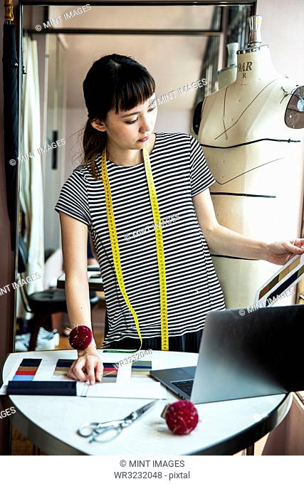 Japanese female fashion designer standing at desk, working in her studio