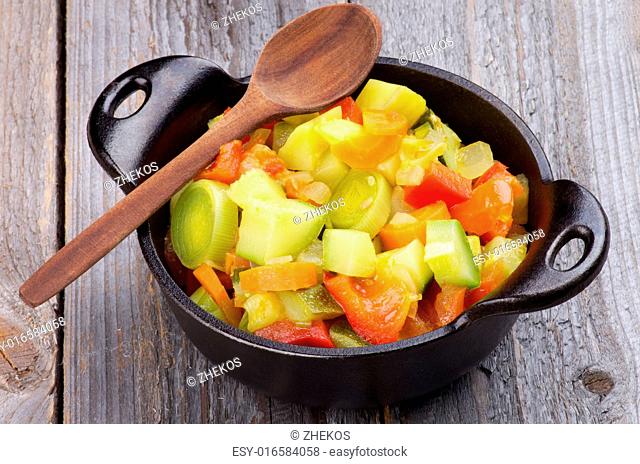 Vegetable Stew with Zucchini and Leek in Black Saucepan with Wooden Spoon isolated on Rustic background