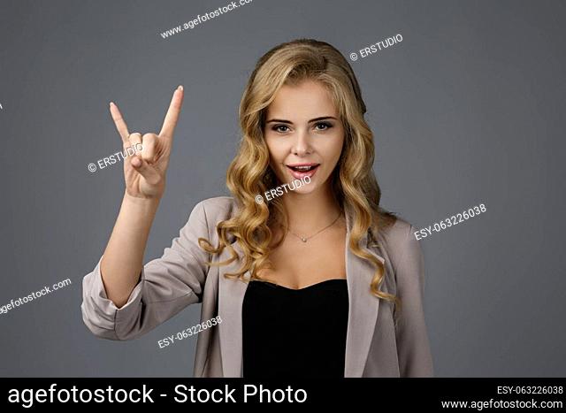 smiling young woman showing rock and roll hand and looking at camera on gray background