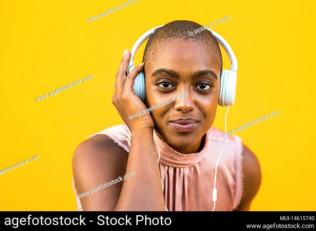 Portrait of dark skinned woman listening to music on headphones over yellow background. Smiling african american lady enjoying her favourite song using wired...