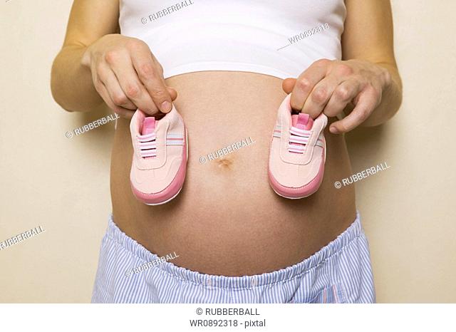 Mid section view of a pregnant woman holding a pair of shoes