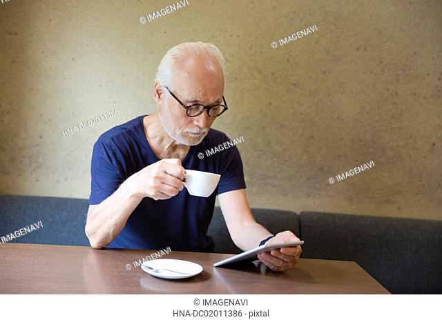 Senior man drinking coffee and using tablet PC