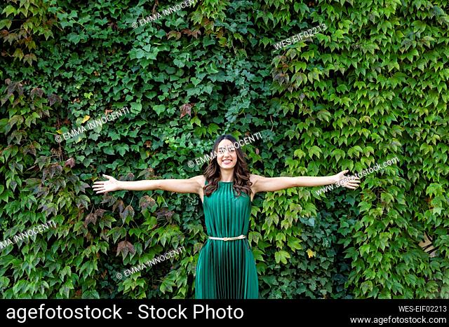 Happy beautiful woman with arms outstretched in front of ivy plants