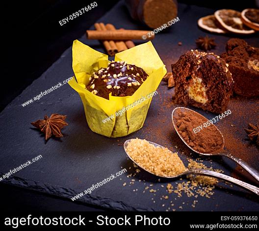 chocolate cake in yellow paper on a black background, next to two iron spoons with sugar and cocoa