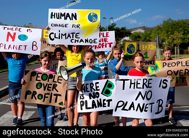 Front view of a diverse group of elementary school pupils walking down a road in the sun on a protest march, carrying signs with environmental and conservation...