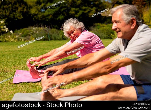 Senior caucasian couple practicing yoga, stretching in sunny garden