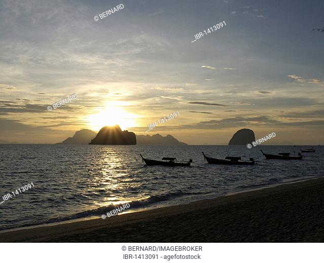 Long tail boats at sunrise with a group of rocks and Ko Muk island in the back, seen from the beach of Ko Hai island, Ko Ngai, Andaman Sea, Satun Province