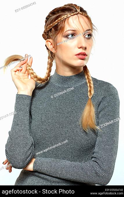 Portrait of beautiful young dark blonde woman. Female with creative braid hairdo on gray background. Girl holds braid in hand
