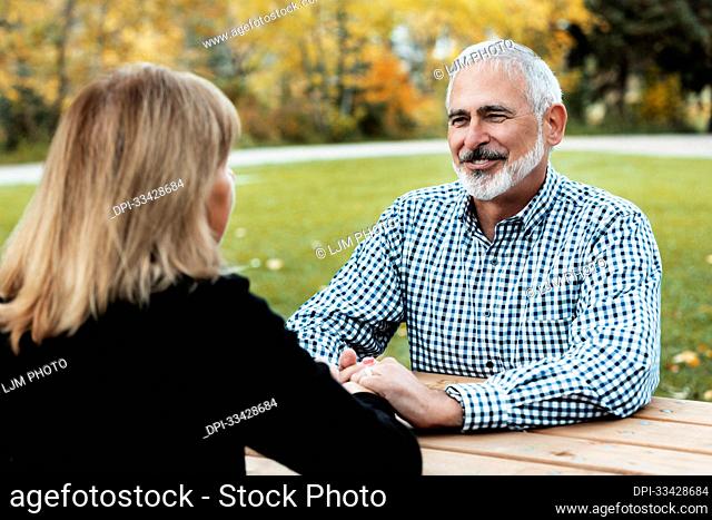A mature couple holding hands at a picnic table after spending some quality time discussing their relationship; St. Albert, Alberta, Canada