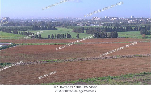 Aerial of fields and orchards; rural landscape. City or urban area in background
