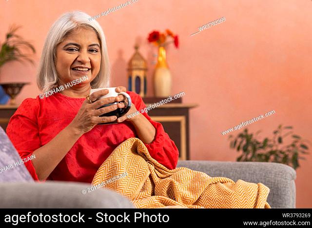 Portrait of an old woman drinking tea in living room