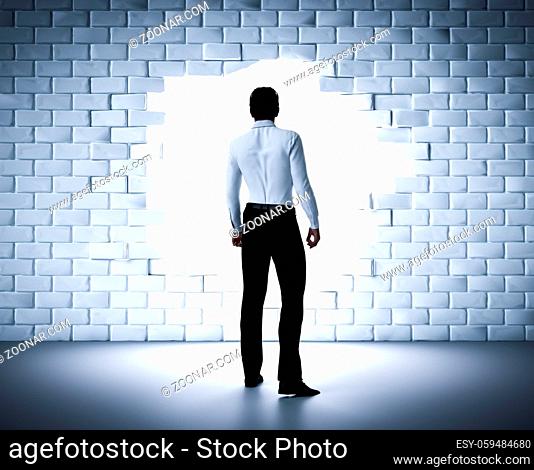 Businessman standing next to a hole in a brick wall. Light coming from outside. Concept of a change, new career, breaking the obstacle. 3D rendering