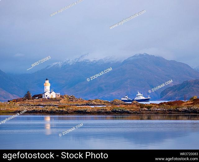 Lighthouse on Isle of Ornsay, the southern side of Isle of Skye, Scotland. Trade ship at rocky island, mountains in background