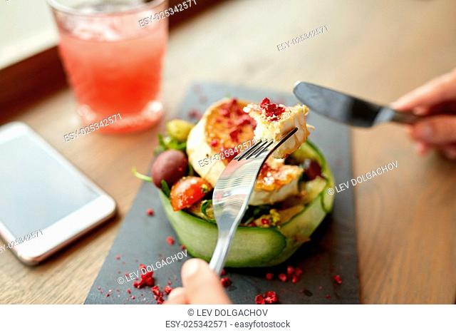 food, culinary, haute cuisine and people concept - woman eating goat cheese salad with vegetables and dried raspberries using fork and knife at restaurant or...