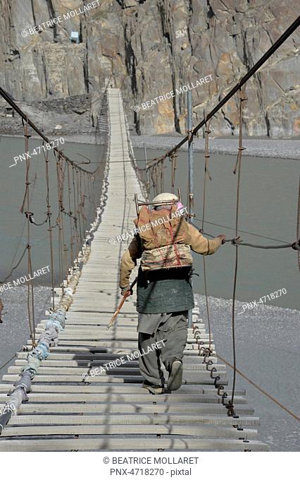 Pakistan, Gilgit Baltista area, Passu, a man is crossing the Hunza river on the Hosseini suspension bridge