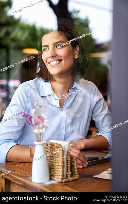 Portrait shot through window of smiling Latin-American woman sitting at cafe