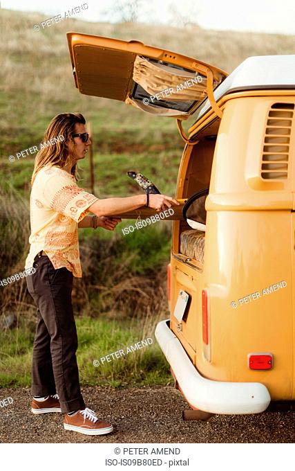 Young male surfer removing surfboard from vintage recreational vehicle, Exeter, California, USA