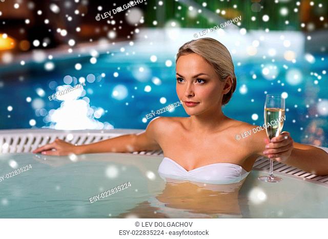 people, beauty, spa, healthy lifestyle and relaxation concept - beautiful young woman wearing bikini swimsuit sitting with glass of champagne in jacuzzi at...