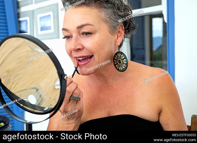 Mature woman applying lipstick sitting in front of mirror at home