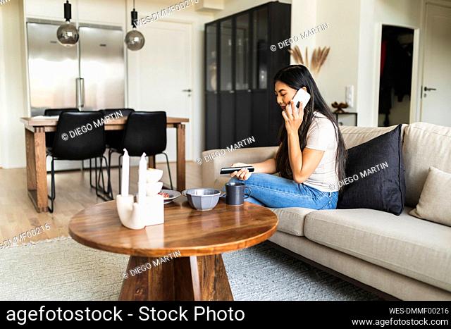 Woman talking on smart phone sitting on sofa at home
