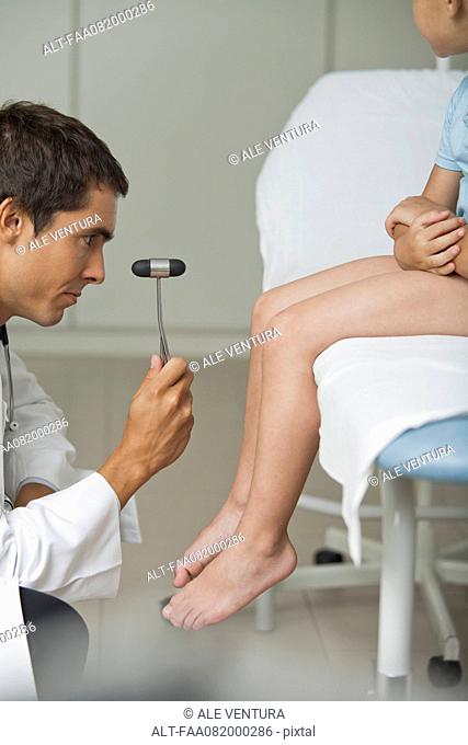 Doctor checking boy's reflexes with reflex hammer, side view, cropped